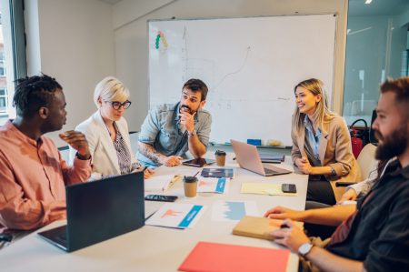 Happy multiracial business team working together at corporate briefing gathered at table in the conference room. Smiling diverse colleagues in a boardroom discussing business together.