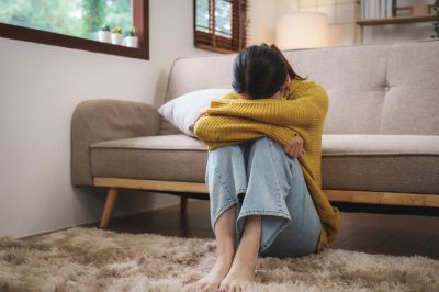 Young Asian woman suffering from work stress sits alone on the sofa at home discouraged. Desperate Asian woman feeling lonely, resilienz Training, Nerven beruhigen, Stress, Burnpou