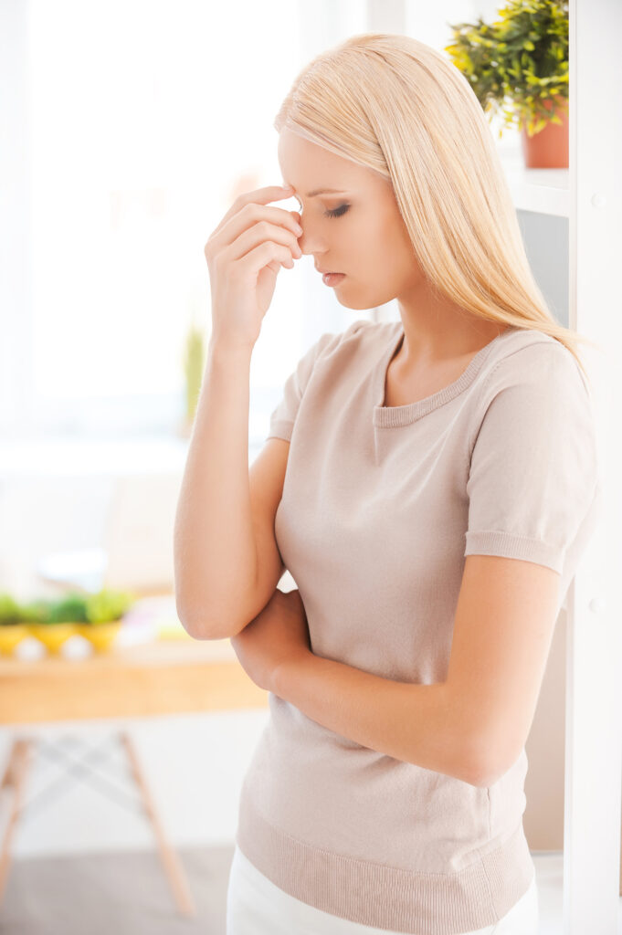 Too much stress. Frustrated young woman touching her nose and keeping eyes closed while standing in office and near her working place Stress, Stressor