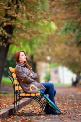 Style redhead girl sitting at bench in autumn park.